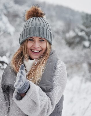 Conception of winter holidays. Cheerful girl in warm clothes playing with snow outdoors near the beautiful forest.